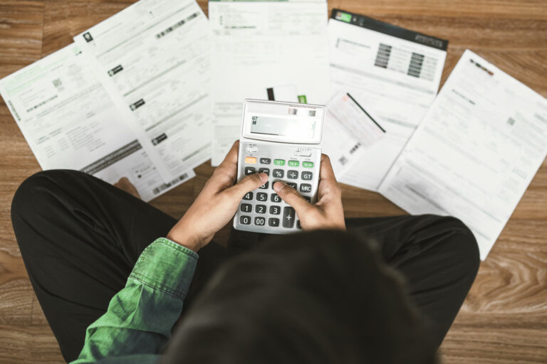 pessoa sentada no chão fazendo cálculos em calculadora com várias faturas e boletos demonstrando boas práticas financeiras