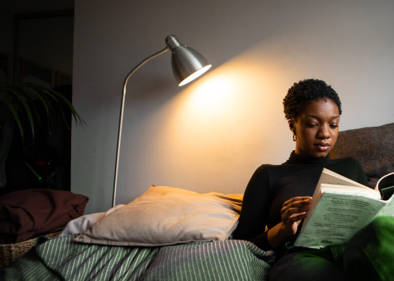 Mulher sentada no sofá enquanto lê um livro sobre investimentos.