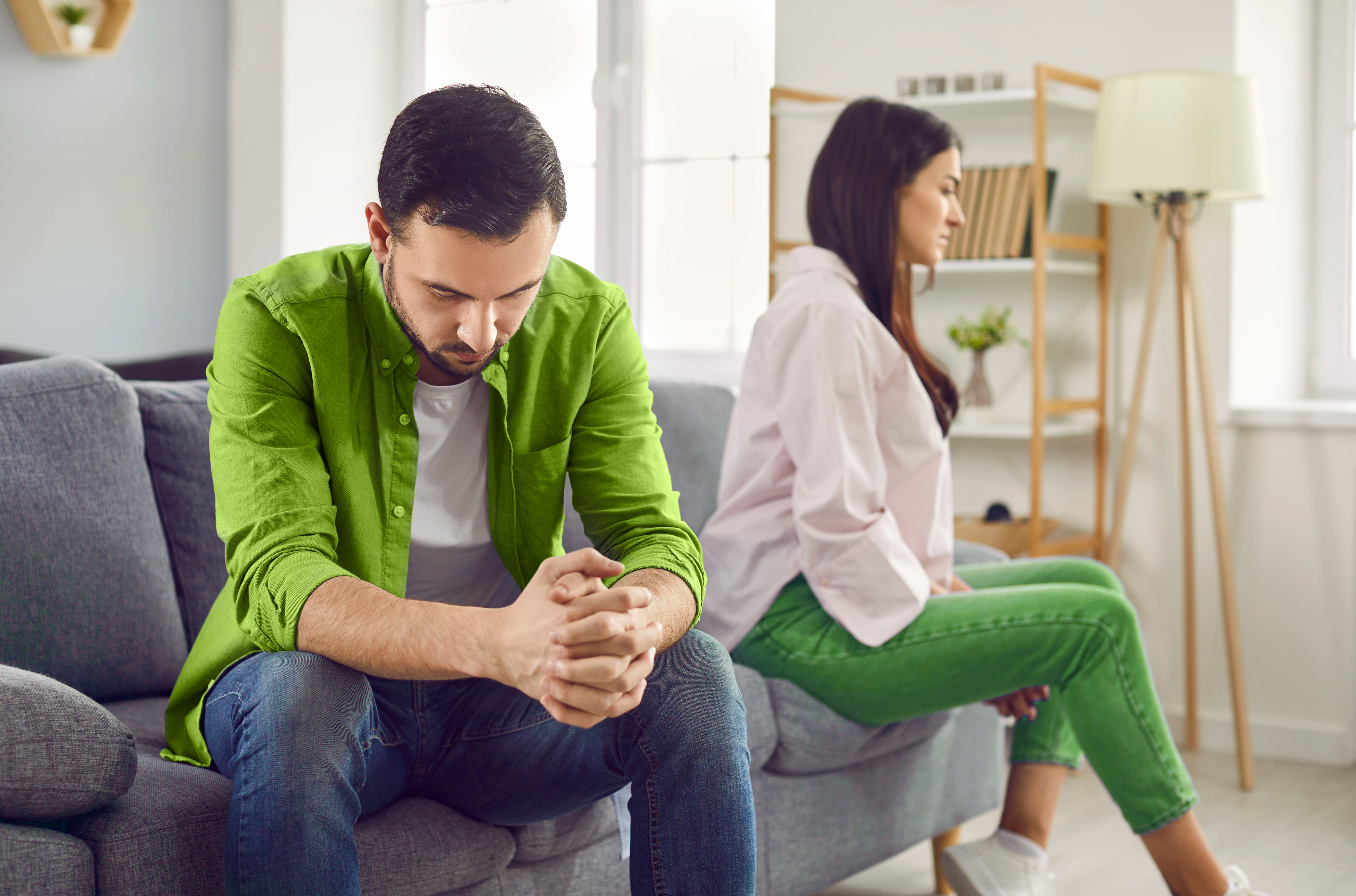 homem triste sentado no sofá de uma sala ao lado da sua esposa, que está de costas pra ele