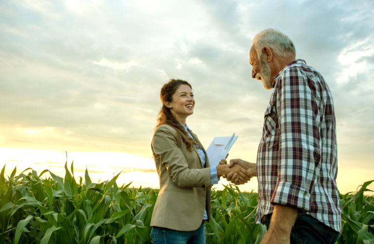 produtor rural fechando acordo com agente de crédito por produto de crédito rural com plantação ao fundo e céu com nascer do sol.