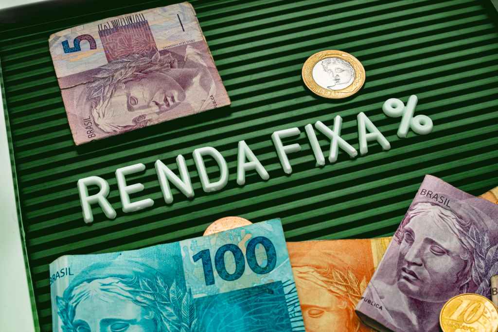Notas de 5 e 100 reais em um fundo escuro com o texto “RENDA FIXA” em letras brancas no centro da imagem.