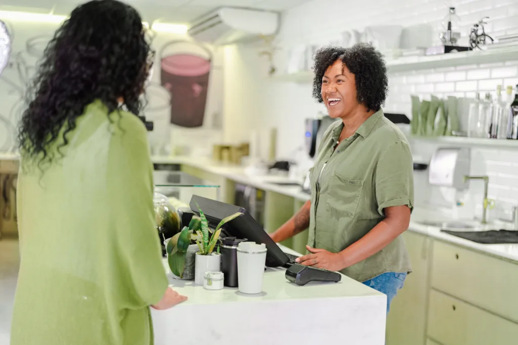 Mulher no caixa sorrindo e atendendo outra mulher em uma microempresa